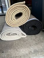 Three rolled rugs stacked, showing backing and edges