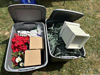 Overview of both totes and contents: faux poinsettias, evergreen branches, white lantern, lights, boxes.