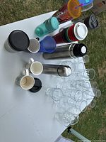 Overview of all glassware, travel mugs, tumblers, ceramic cups and lids on table