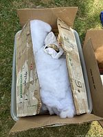 Plastic bin with cardboard inserts and fiberfill containing wrapped nativity figurines, one gold-toned figure partially visible