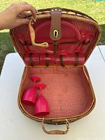 Open wicker picnic basket showing interior gingham lining, plates, cups, goblets, utensil