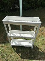 Front view of three-tier white plastic shower caddy outdoors