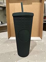Front view of dark green studded tumbler standing upright