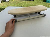 side view of mini ironing board on table, showing fabric cover, metal frame, collapsible legs