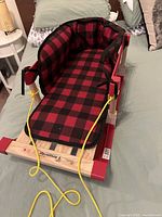 Side view of sled showing wood frame, red runners, padded seat and pull rope