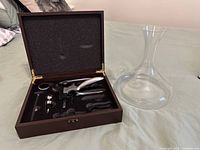 Open wooden case showing corkscrew kit and glass decanter