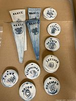 Group of tapered stake and round disc ceramic markers showing herb names and motifs