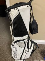 Full side view of PING white/black Hoofer stand bag showing pockets, logo, and leg mechanism