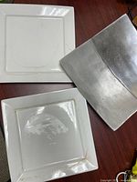 Two white square plates showing staining and one plate edge