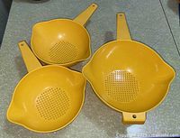 Top view of three yellow Tupperware strainers showing sizes and perforations