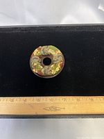 Front view of brooch displaying multicolor and gold-leaf design with ruler for scale
