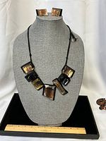 Necklace displayed on bust with matching earrings at top and ruler at base for scale