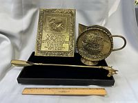 Full view of all three brass items on black base with ruler for scale