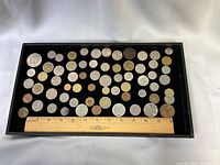 Full tray with approximately 60 assorted coins and tokens next to 12-inch ruler for scale