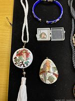 Overview of round tassel pendant necklace, blue bangle, small teardrop pendant in case and teardrop bird pendant