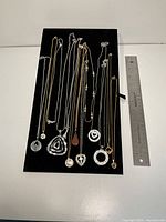 Full view of all fourteen necklaces on display board next to 12-inch ruler for scale