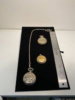 Overall view of three pocket watches and chain next to ruler for scale
