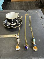 Overall lot showing teacup, saucer, three necklaces with ruler for scale