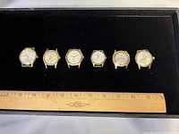 Overview of six gold-tone watch heads with ruler for scale