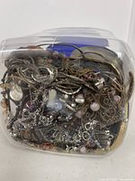Side view of plastic jar packed with tangled costume necklaces