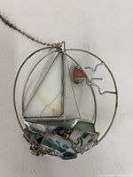 Full view of stained glass sailboat suncatcher showing white sail, green agate pieces, pink stone, metal frame