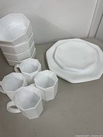 Stacked bowls, mugs, plates showcasing octagonal shape and milk glass material
