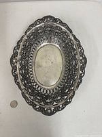 Top view of silver-plated oval pierced basket bowl beside coin for scale