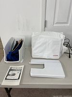 Sewing machine cover, accessory bin with contents, extension table, instruction book