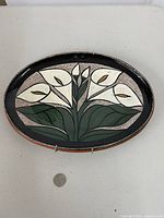 front view of oval painted clay wall hanging with calla lilies, coin for scale