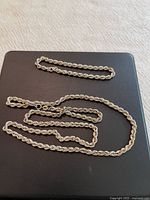 Necklace and bracelet coiled on black surface showing rope twist pattern