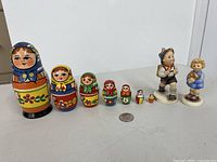 Full lot showing seven nesting dolls, two Hummel figurines and coin for scale