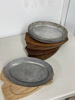 Stack of four metal plates on four dark wooden boards plus one metal plate on light board