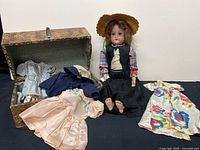 Doll seated beside trunk with clothing laid out