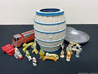 Group shot of all items including porcelain figurines, barrel bank, die-cast vehicles and metal tray