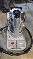 Top front view of Conair garment steamer showing base, control panel, chrome panels and attached hose