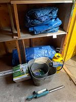 All items together: hedge trimmer, sprayer, buckets, boxed lights, tarps on shelf