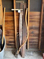 Tall two-man crosscut saws, scythe handle, barn pulley, axe handle visible against wall