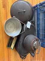 Grouped view of cast iron lids, oval roaster, kettle, aluminum pail, straight razors