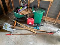 Assortment of wheelbarrow, garbage bin, gas can, long-handle tools on floor