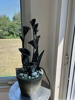 Full view of fountain near window showing pot, stones, and metal cups