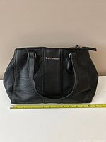 Front view of black faux leather Enzo Angiolini purse with measuring tape for scale