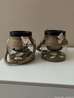 Front view of both lanterns showing glass bodies, jute accents, handles and tags