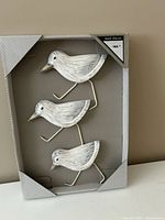 Front view of packaged set showing three whitewashed wooden birds with metal legs