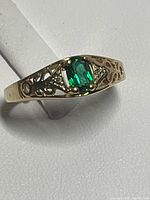 Ring top view showing green center stone, filigree design and diamond chips