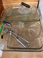 Stack of rectangular glass baking dishes with plastic measuring cup, Pyrex glass measuring cup and manual hand mixer on top