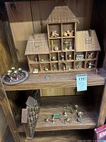 Overall view of large wooden house shelf filled with brass miniatures and additional pieces on surrounding shelf.