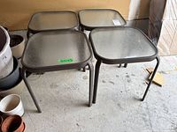 Four matching square metal and glass side tables grouped together