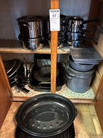 Cabinet view showing multiple stainless pots, fry pans, grey enamel stock pots and stacked roasters