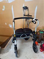Front view of Evolution Xpresso Lite rollator with seat and basket, crutches and canes behind