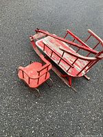 Top view of two red sleighs showing size difference, construction details, paint wear